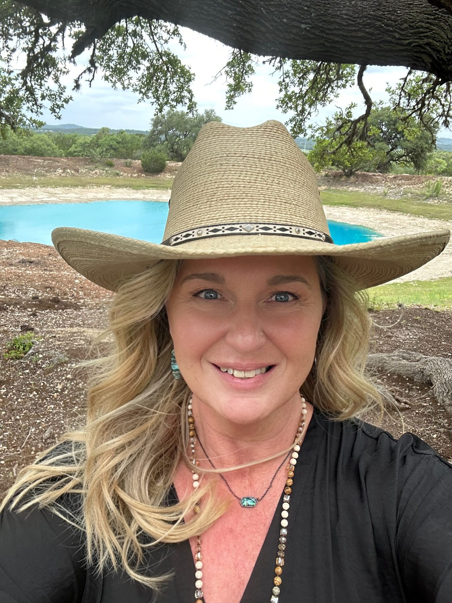 Deborah Woytek in a straw hat in front of a ranch pond